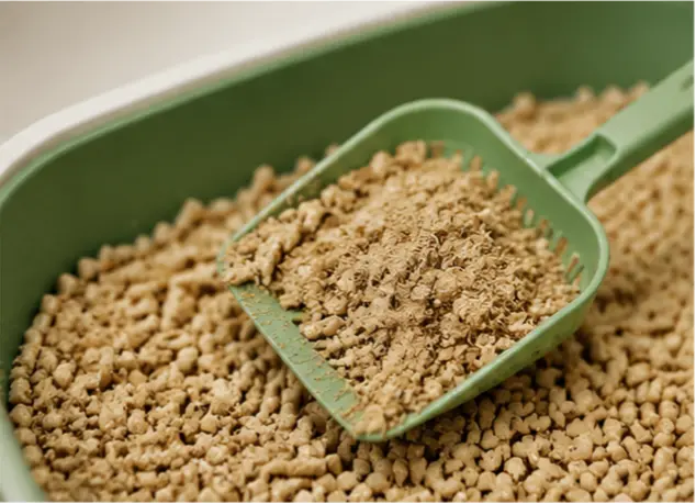 Green scoop removing used pine cat litter from a litter box with wood pellets